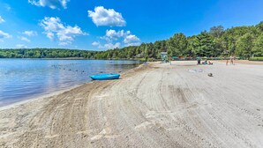 A beach with a boat, people, and a forested hill in the background. - Game Room & Fire Pit: Tree-lined Pocono Lake Cabin (Pocono Lake)