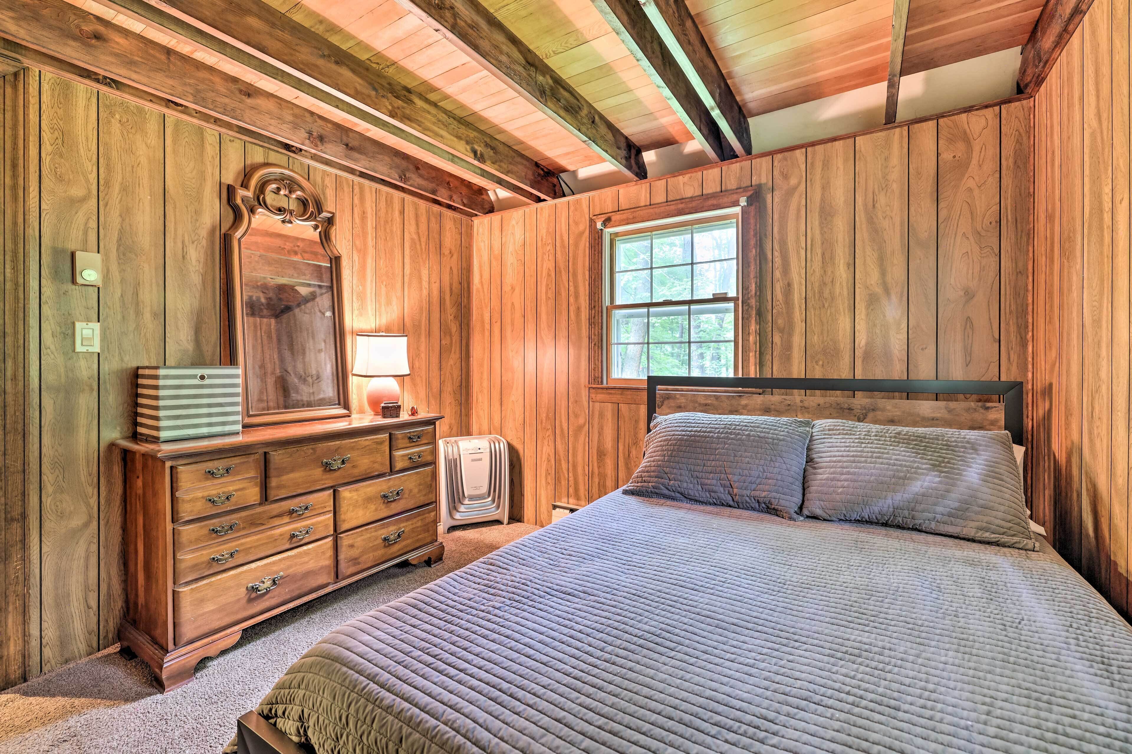 Un dormitorio con paneles de madera, una cama, un tocador, un espejo y una ventana.