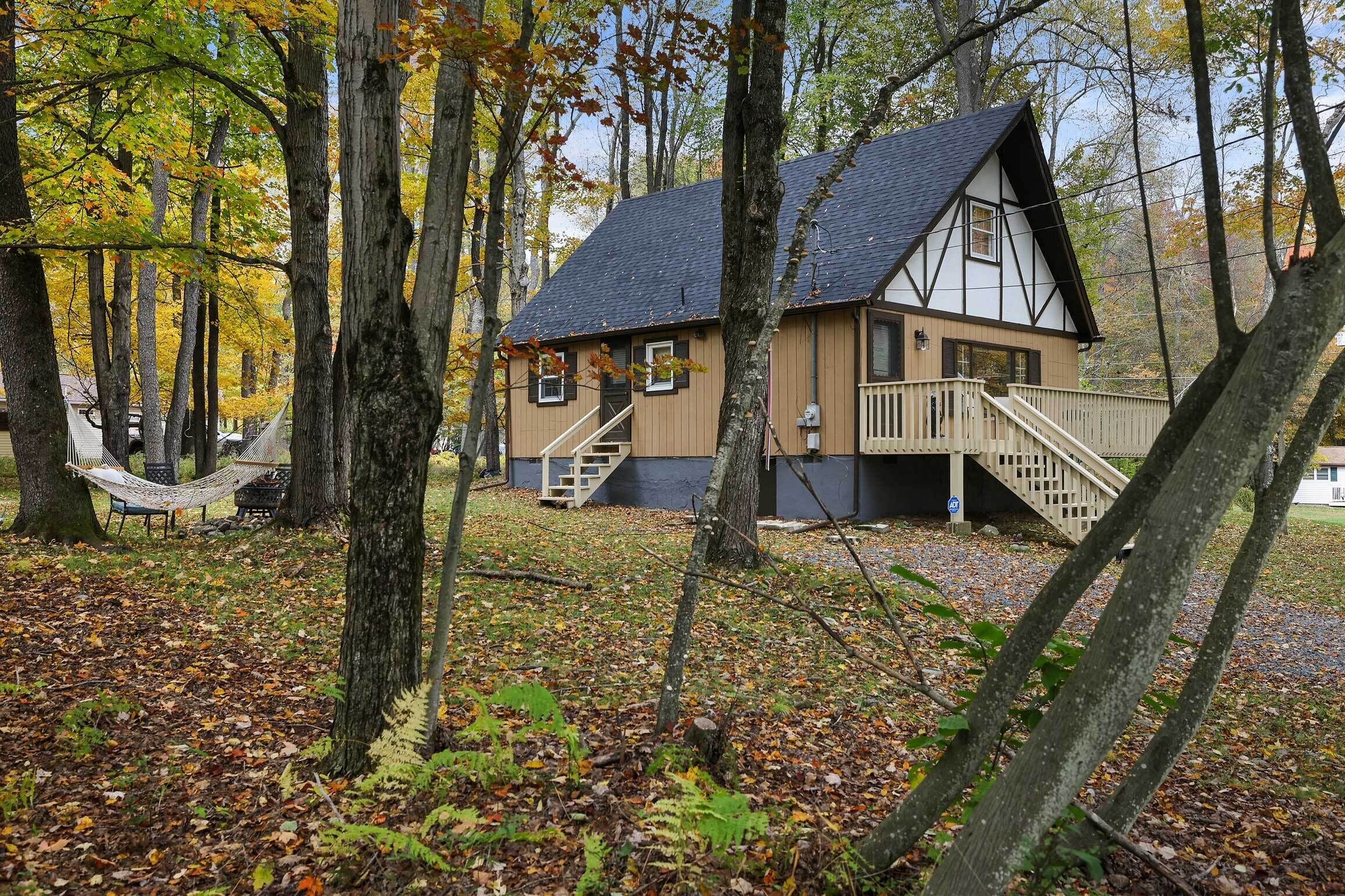 A cabin with a staircase leading to a deck, surrounded by trees and a hammock.