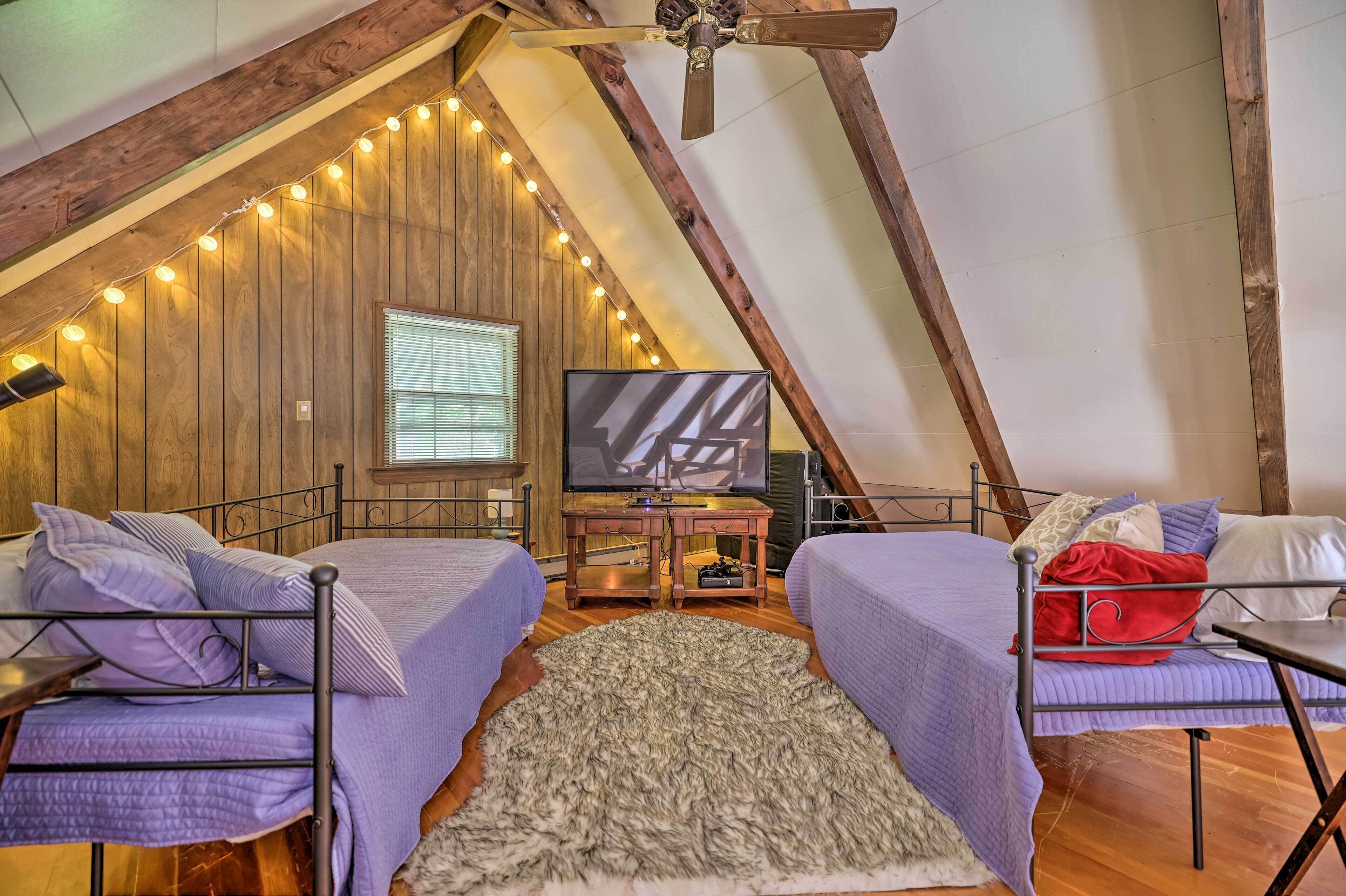 A cozy attic bedroom with two beds, a TV, and string lights.