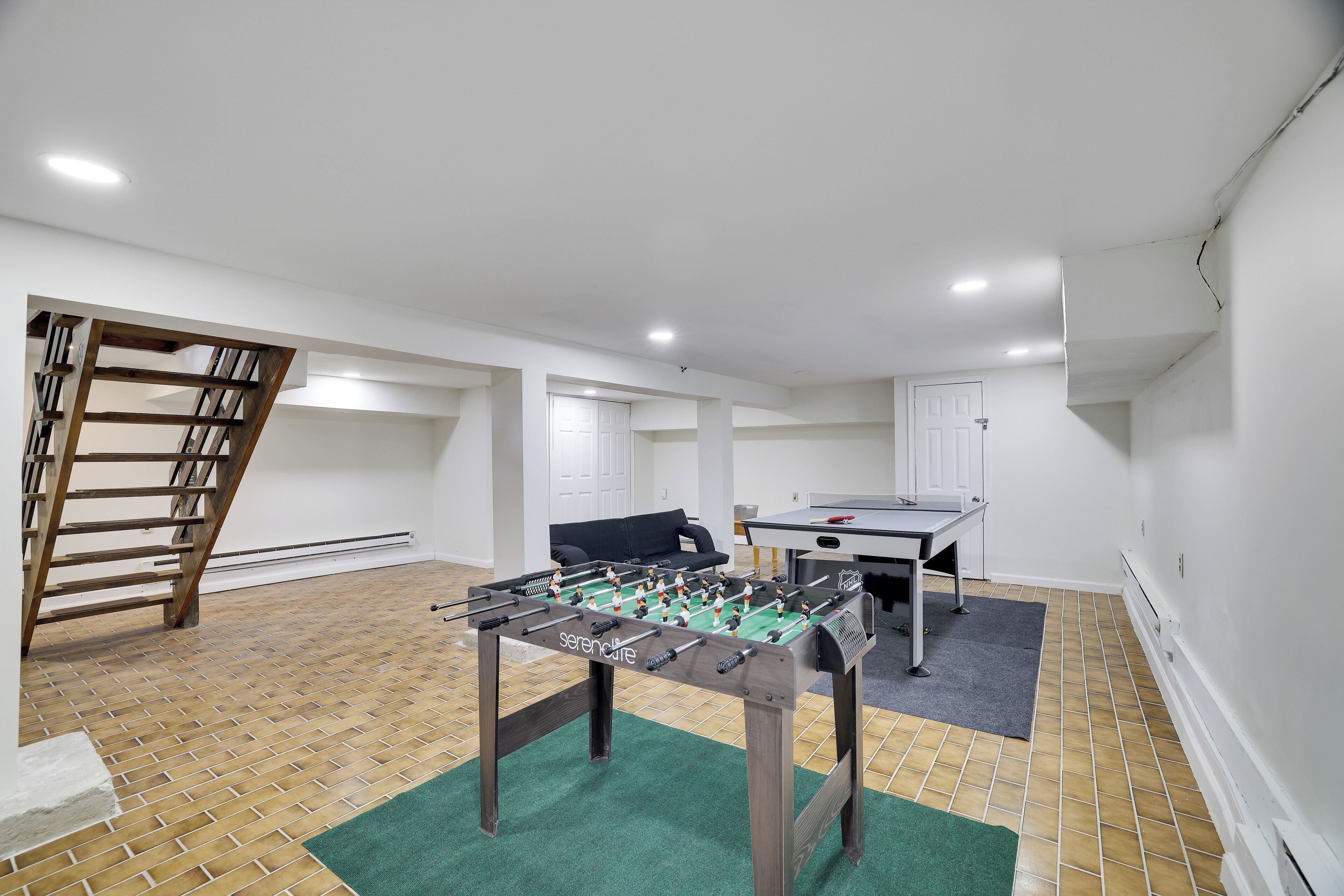 A room with a foosball table, a ping pong table, and a sofa.
