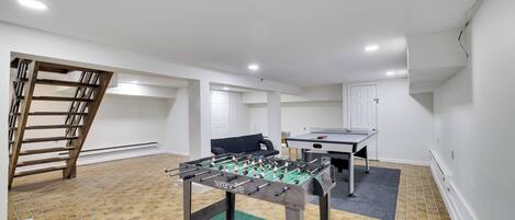 A room with a foosball table, a ping pong table, and a sofa.