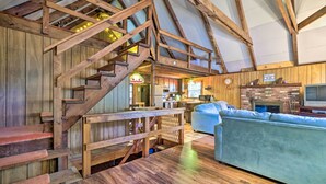 A rustic interior with wooden floors, a staircase, a sofa, and a kitchen area. - Game Room & Fire Pit: Tree-lined Pocono Lake Cabin (Pocono Lake)