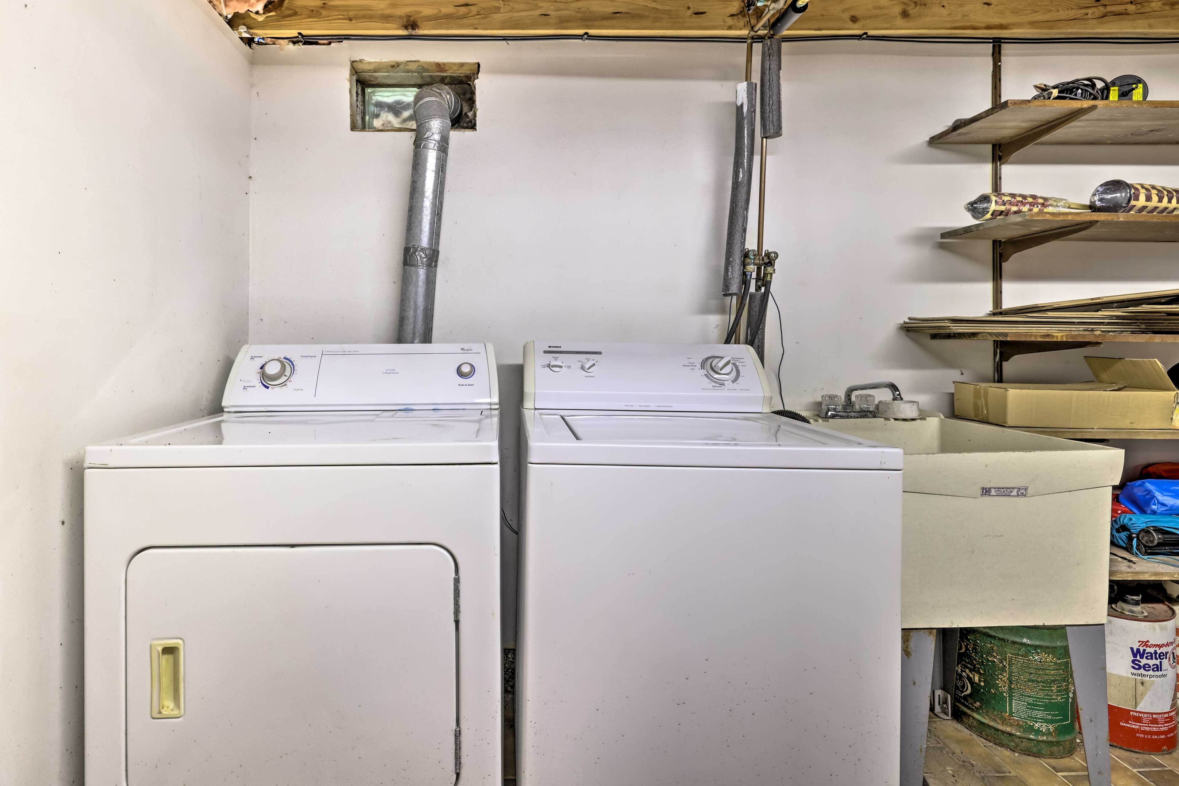 A laundry room with two stacked washers and dryers, a metal vent, and a shelf with various items.