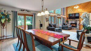 A spacious living room with a wooden dining table, blue upholstered chairs, a fireplace, and a large TV.