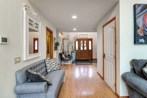 A hallway with a grey sofa, a wooden floor, and a door with a sign above it.