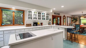 A modern kitchen with white cabinetry, a central island, and a dining area with a 'WELCOME' sign.