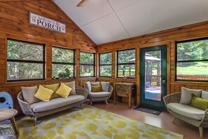 A wooden porch with a welcome sign, wicker furniture, and large windows.