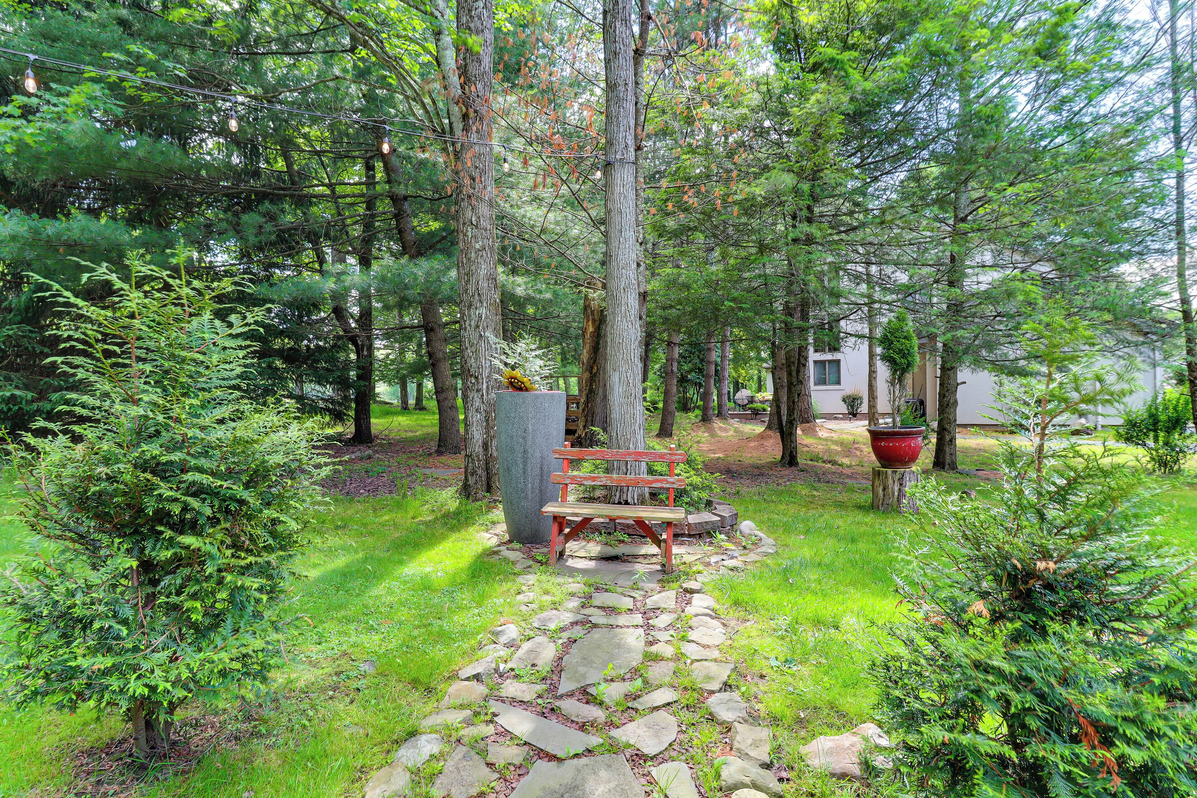 A stone pathway leading to a wooden bench surrounded by lush greenery and trees.