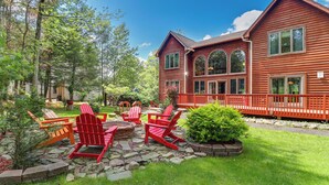 A large wooden house with a stone patio and red Adirondack chairs.