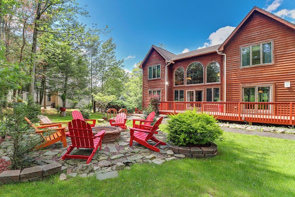 A large wooden house with a stone patio and red Adirondack chairs.