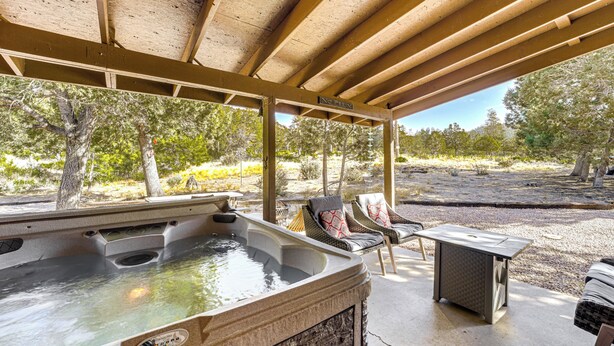 Een hottub onder een houten pergola met stoelen en een tafel, omringd door bomen.