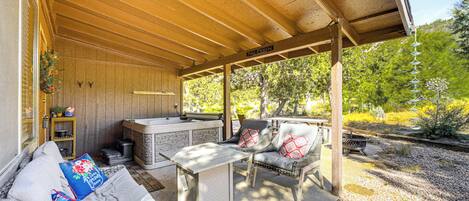 An outdoor covered patio with a grill, seating area, and a view of the surrounding greenery.
