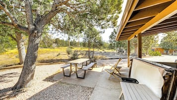 Une terrasse extérieure avec des tables de pique-nique et des bancs, entourée d’arbres et recouverte de gravier.