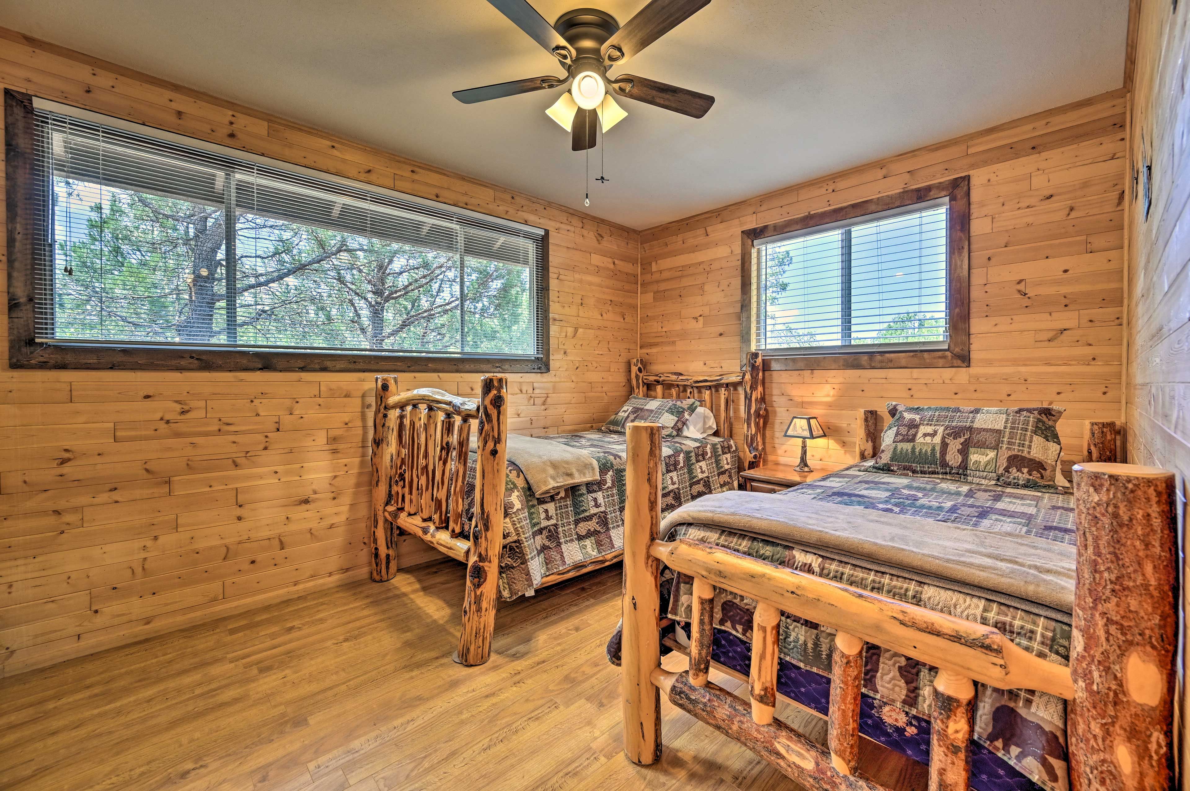 A cabin-style bedroom with two wooden beds, a ceiling fan, and large windows with blinds.