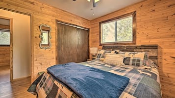 A wooden-paneled bedroom with a bed, a ceiling fan, and a window.