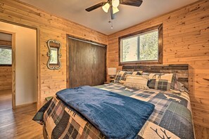 A wooden-paneled bedroom with a bed, a ceiling fan, and a window. - Peaceful Strawberry Cabin: Fire Pit & Hot Tub (Pine)