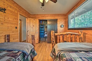 A wooden cabin bedroom with two beds, a closet, and a window with blinds. - Peaceful Strawberry Cabin: Fire Pit & Hot Tub (Pine)