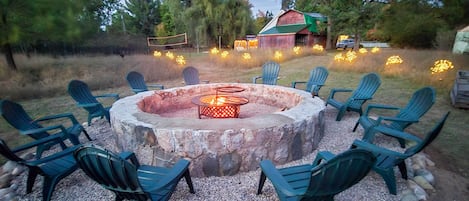 A circular outdoor seating area with a fire pit surrounded by chairs, set on a gravel surface with a stone border.