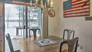 A dining area with a wooden table, chairs, a chandelier, a quilt, and a large American flag on the wall. - Lakefront Phelps Cottage w/ Private Boat Dock (Eagle River)