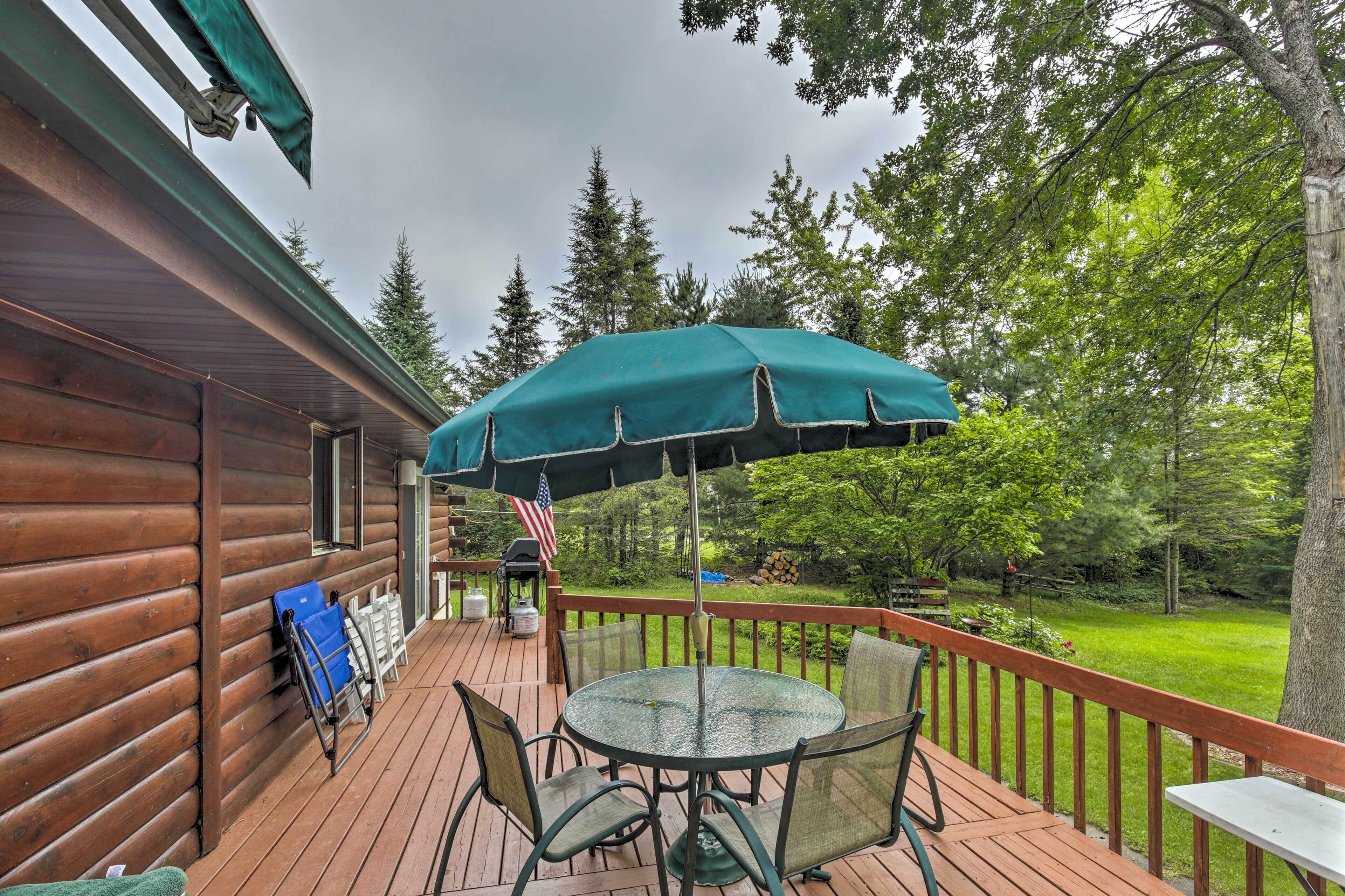 A wooden deck with a table and chairs, an umbrella, and a view of a forested area.