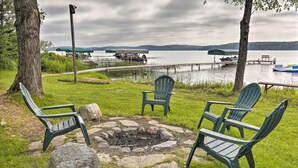 A lakeside seating area with Adirondack chairs, a fire pit, and a dock with boats. - Lakefront Phelps Cottage w/ Private Boat Dock (Eagle River)