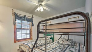 A bedroom with a bunk bed, a window with curtains, a ceiling fan, and a small trash bin. - Lakefront Phelps Cottage w/ Private Boat Dock (Eagle River)