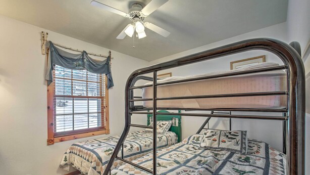 A bedroom with a bunk bed, a window with curtains, a ceiling fan, and a small trash bin. - Lakefront Phelps Cottage w/ Private Boat Dock (Eagle River)
