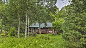 A cabin surrounded by dense forest, with a deck and outdoor seating area visible. - Lakefront Phelps Cottage w/ Private Boat Dock (Eagle River)