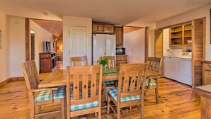 Uma sala de jantar com mesa e cadeiras de madeira, geladeira e cozinha equipada com armários e eletrodomésticos.