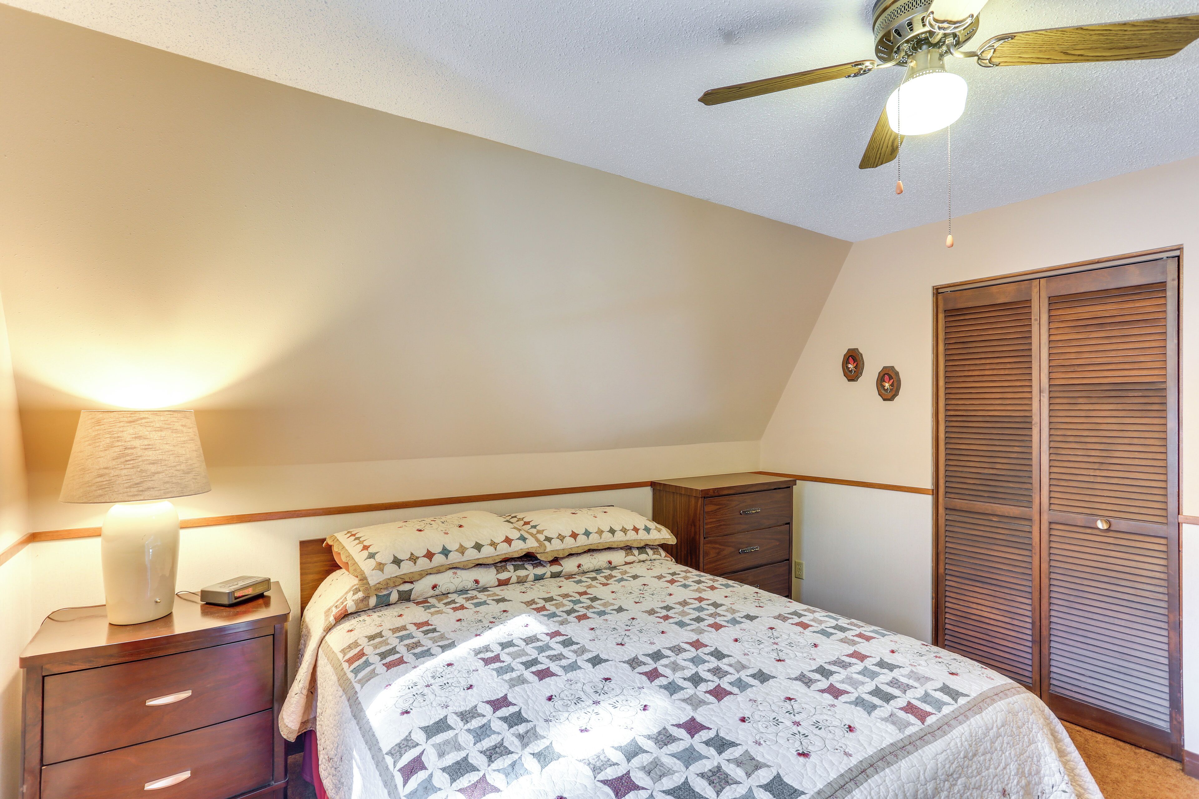 Ein Schlafzimmer mit Bett, Nachttisch, Lampe und Deckenventilator.