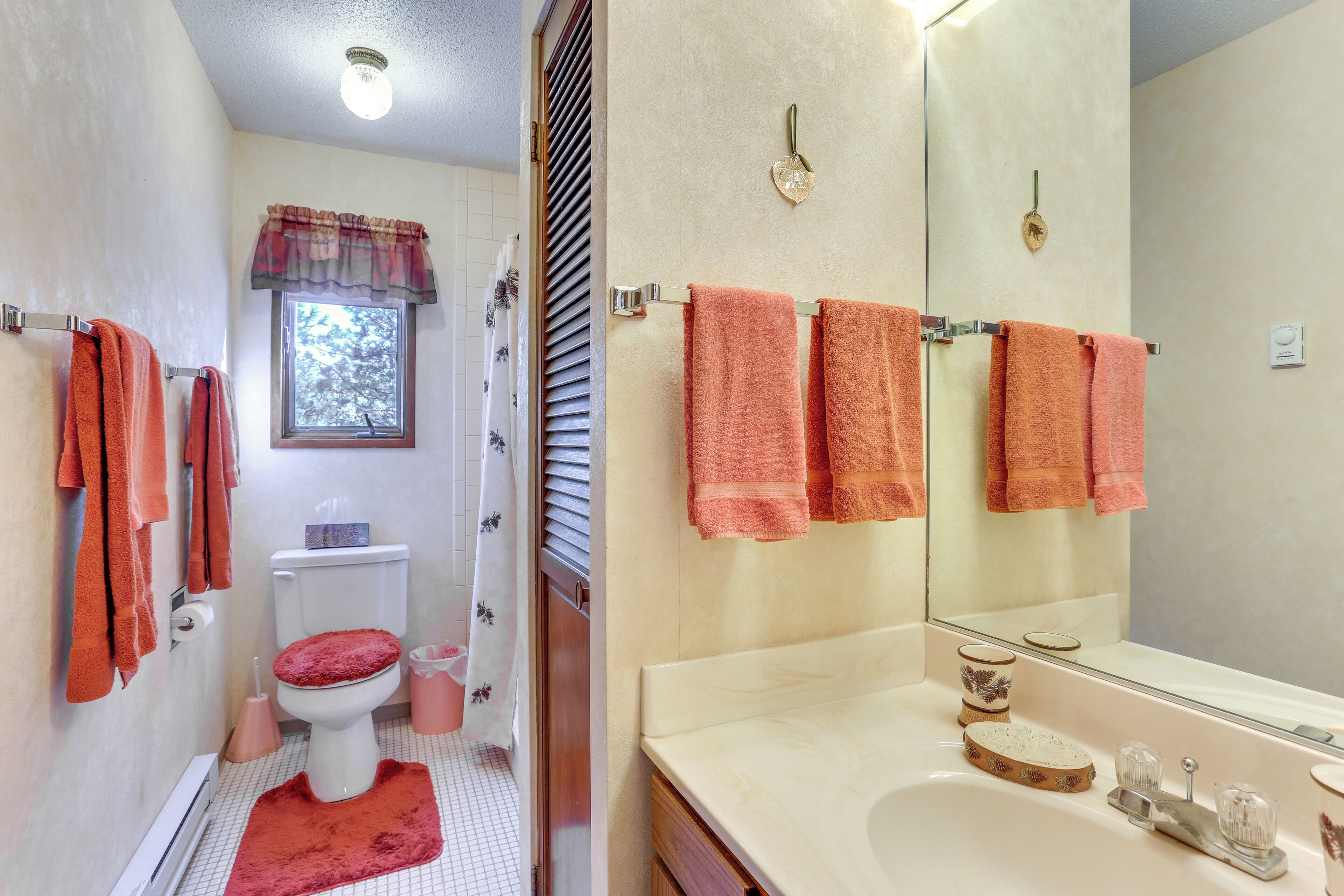 A bathroom with a toilet, sink, and mirror. There are towels hanging on the wall and a window with blinds.