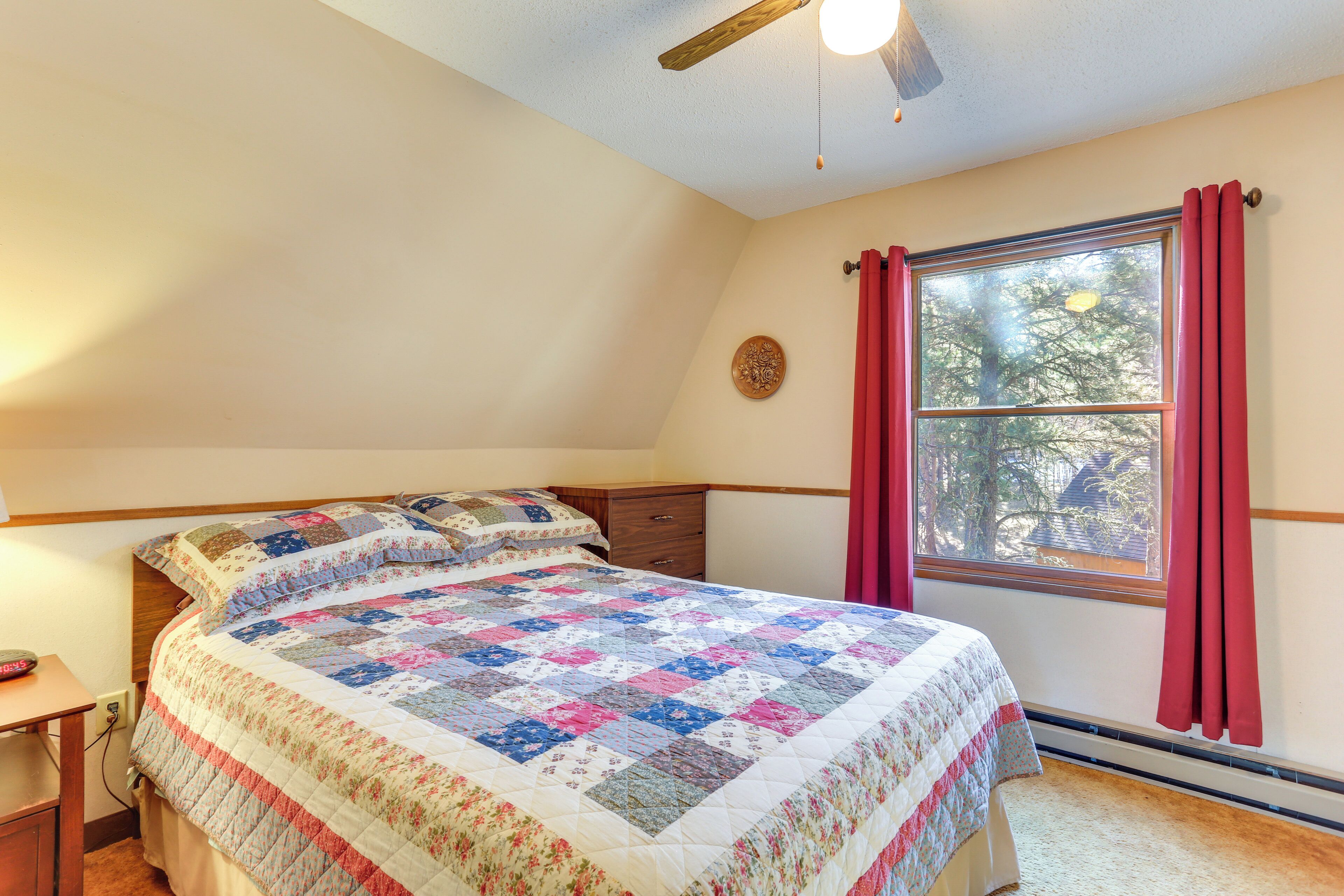 A bedroom with a large bed, a nightstand, a dresser, a window with curtains, and a ceiling fan.