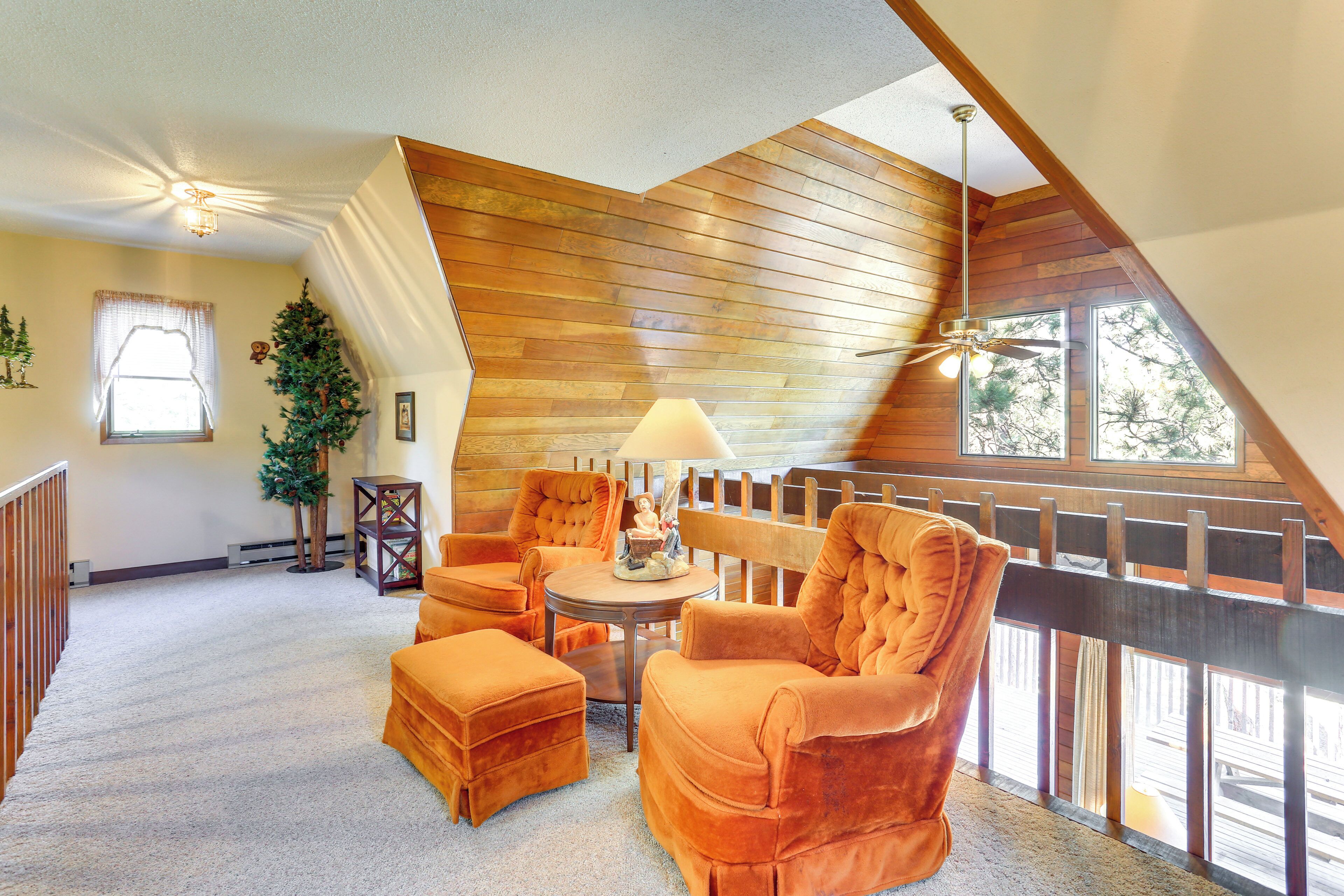 Una habitación acogedora con techo inclinado, paneles de madera, un ventanal grande y una zona de estar con una mesa y sillas.