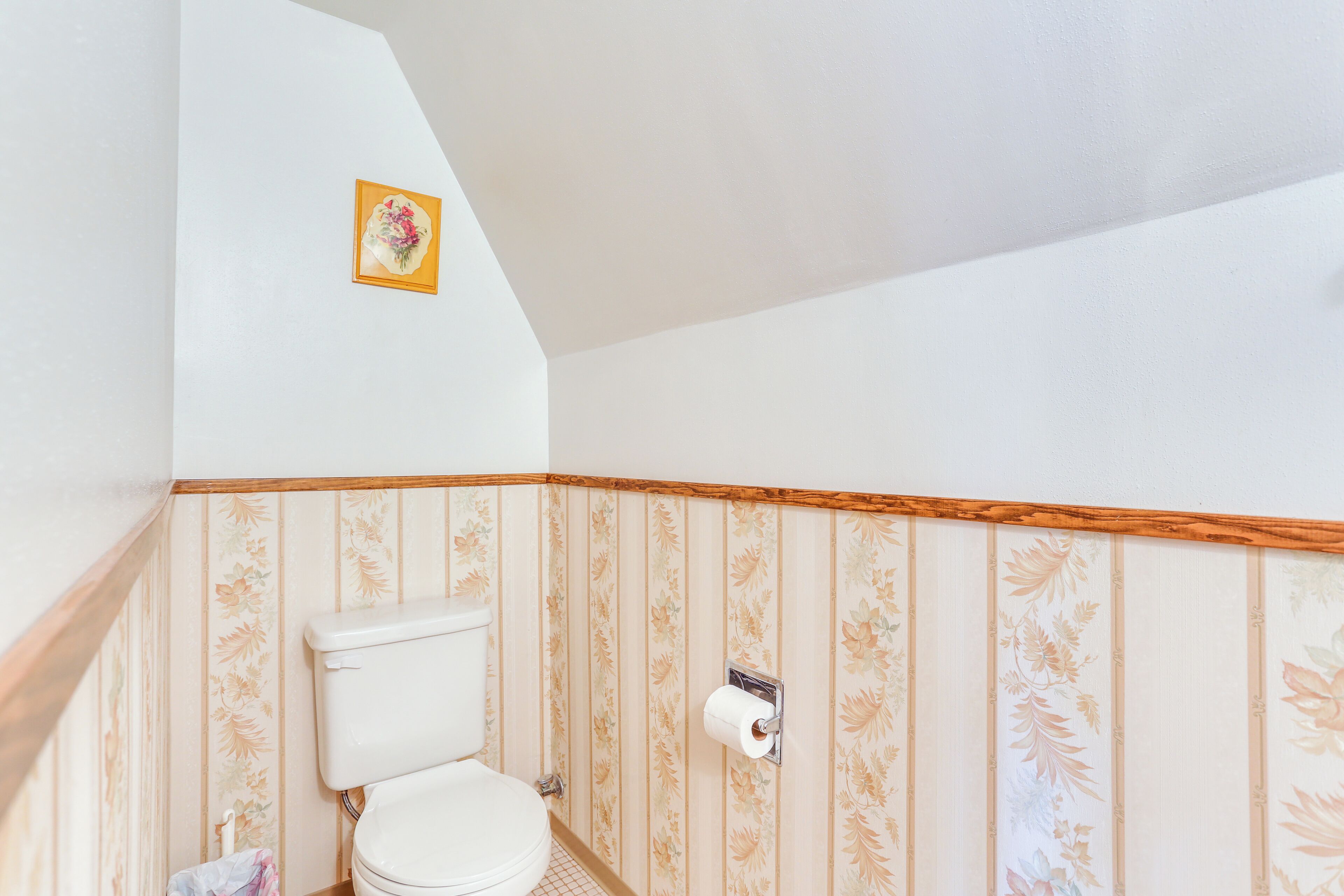 A bathroom with a toilet, a roll of toilet paper, and a floral-patterned wall.
