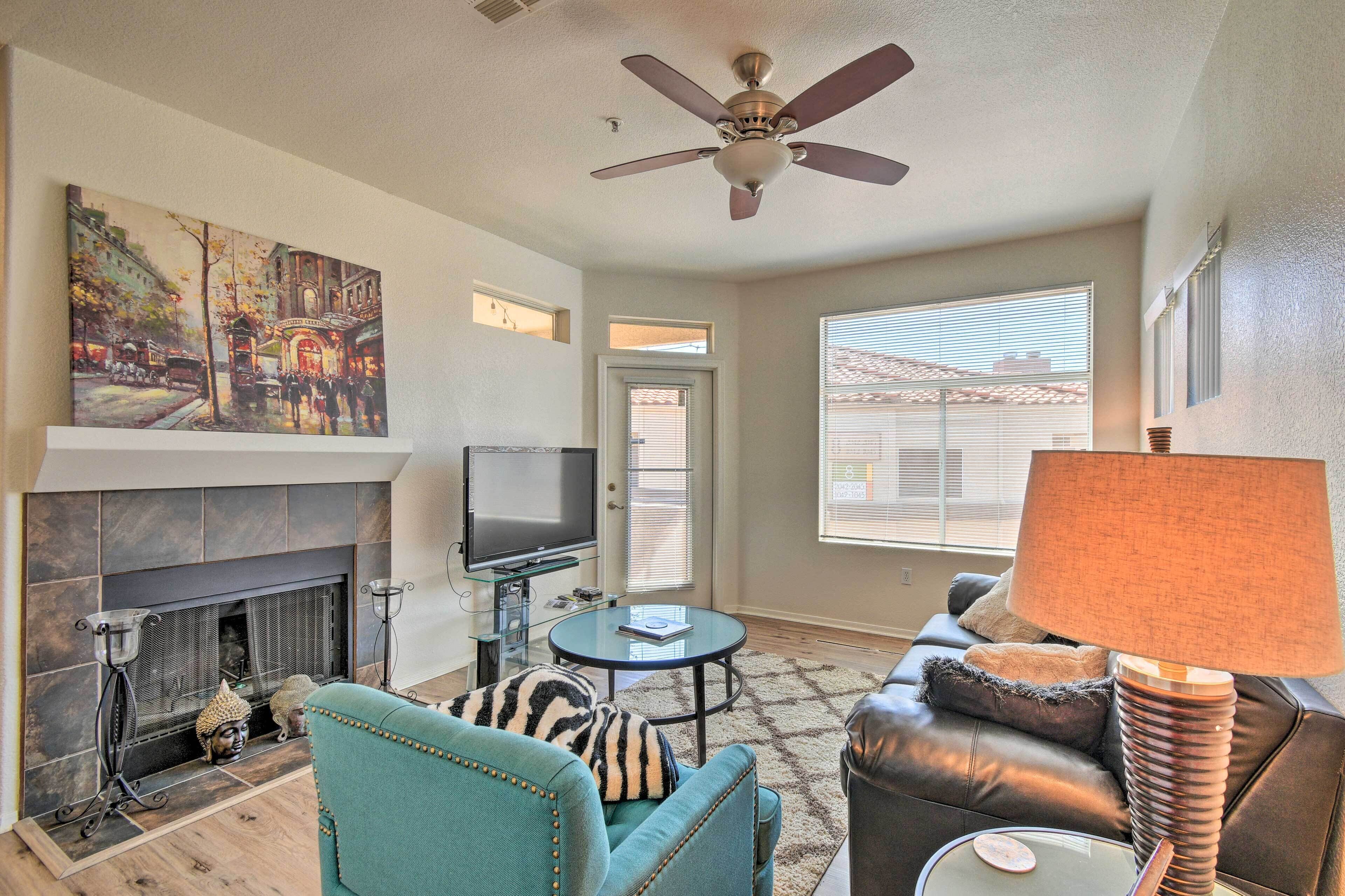 A living room with a fireplace, a television, a ceiling fan, and a large window.