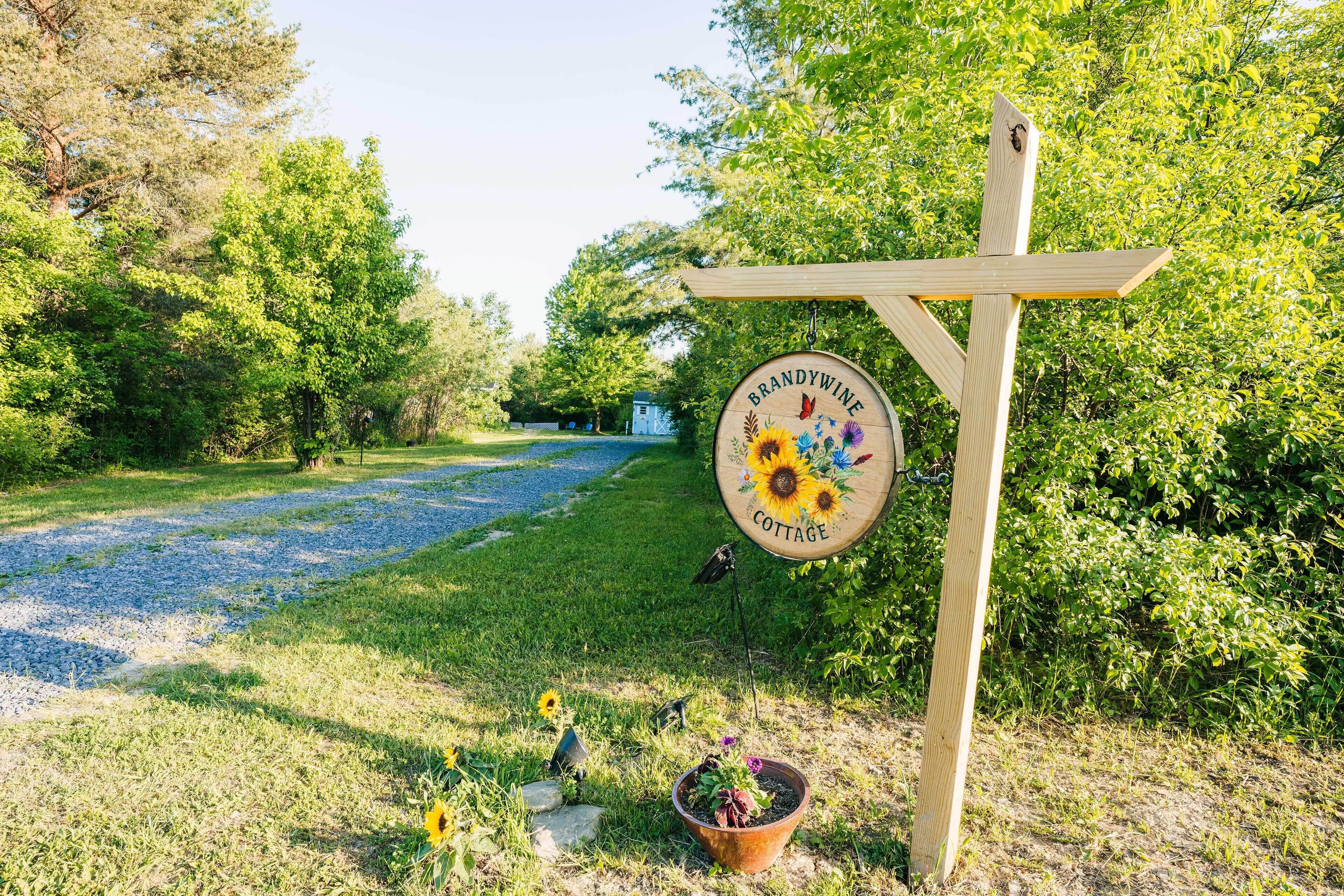 Un cartel de madera con un letrero circular que dice 'BRANDYWINE COTTAGE' e ilustración de un girasol.