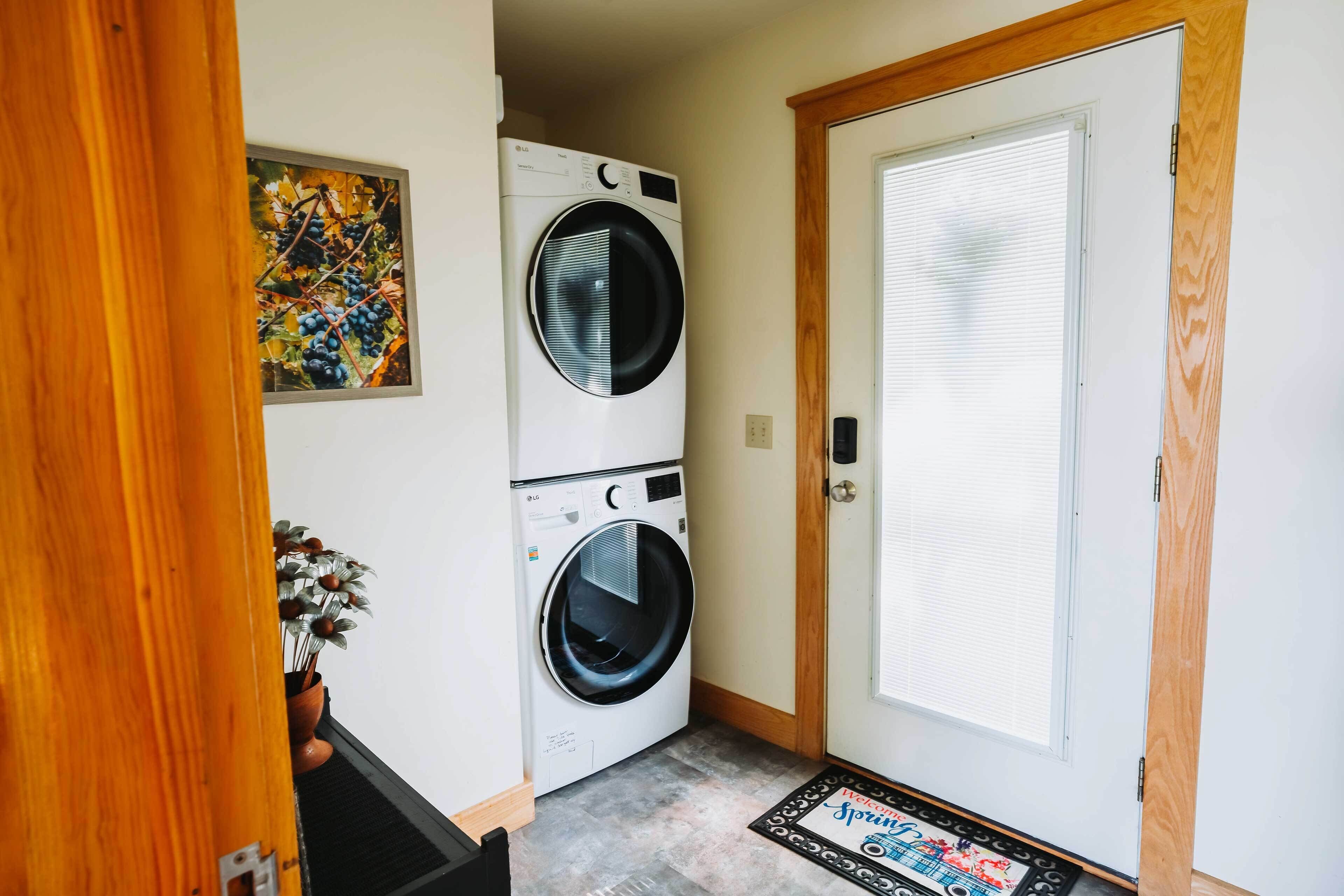 A laundry room with two stacked front-loading washing machines, a wooden door, and a welcome mat.