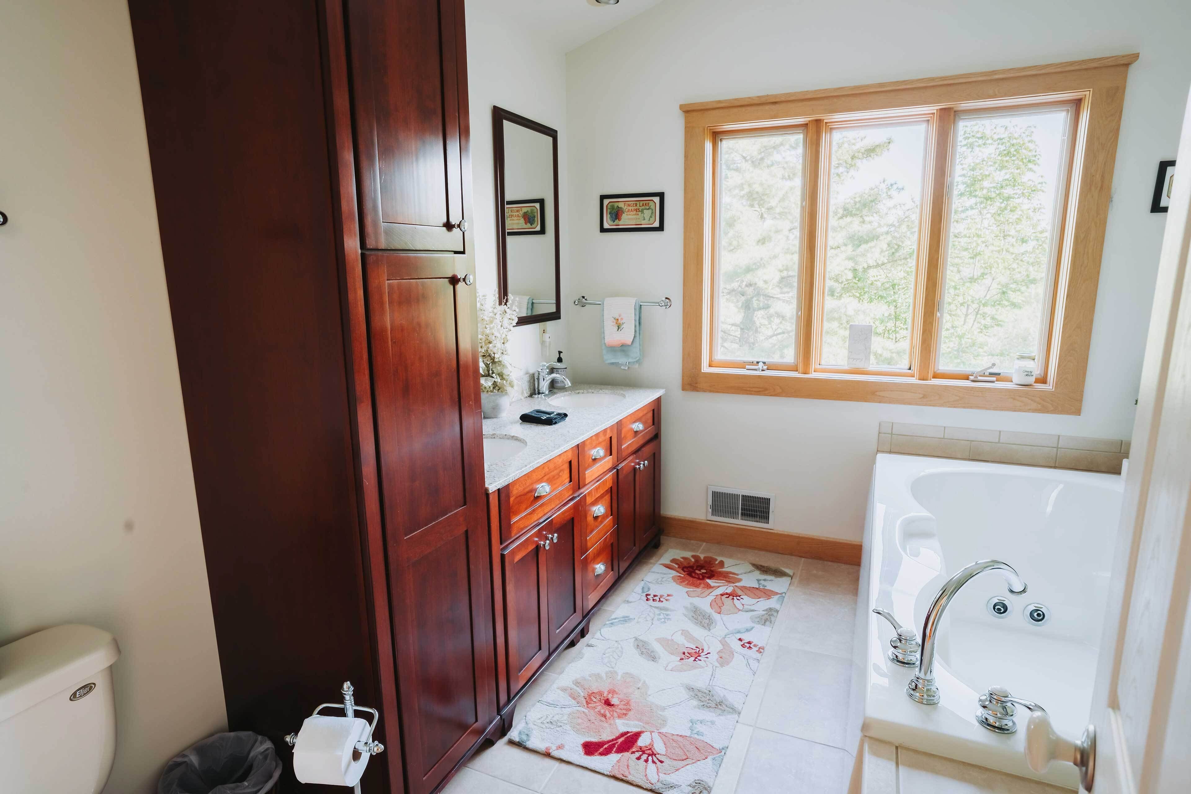 Ein Badezimmer mit Holzwaschtisch, einem großen Fenster, einer Badewanne und einem floralen Teppich.