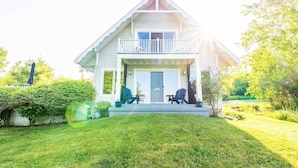 A two-story house with a balcony, a front porch, and a well-maintained lawn. - Finger Lakes Home w/ Private Pool & Lake Views! (Hammondsport)