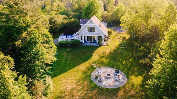 A house surrounded by a lush green forest, with a patio area featuring outdoor furniture and a fire pit. - Finger Lakes Home w/ Private Pool & Lake Views! (Hammondsport)