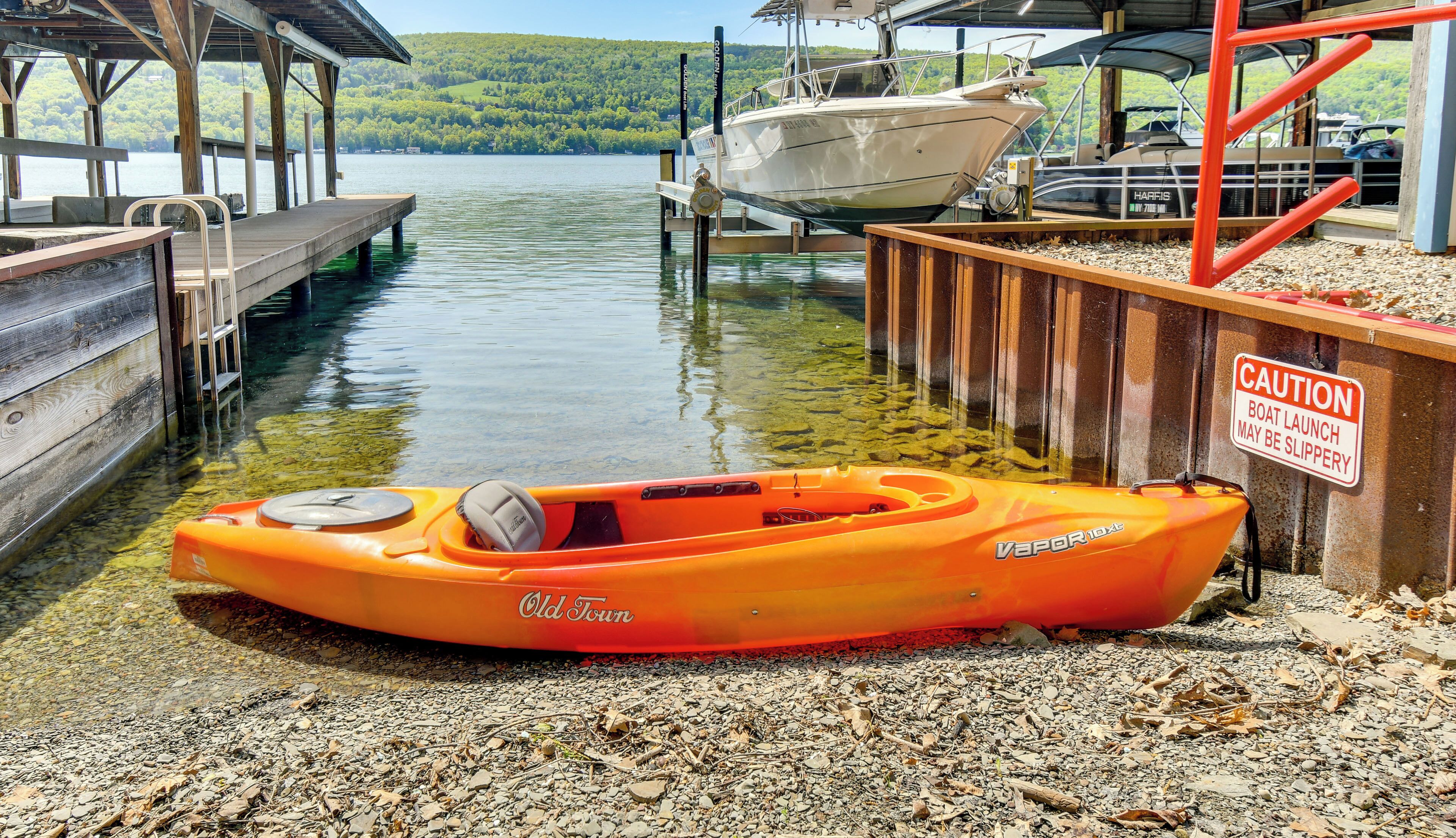 A kayak named 'Old Town Vapor 10x' docked at a pier with a caution sign warning of a slippery boat launch.