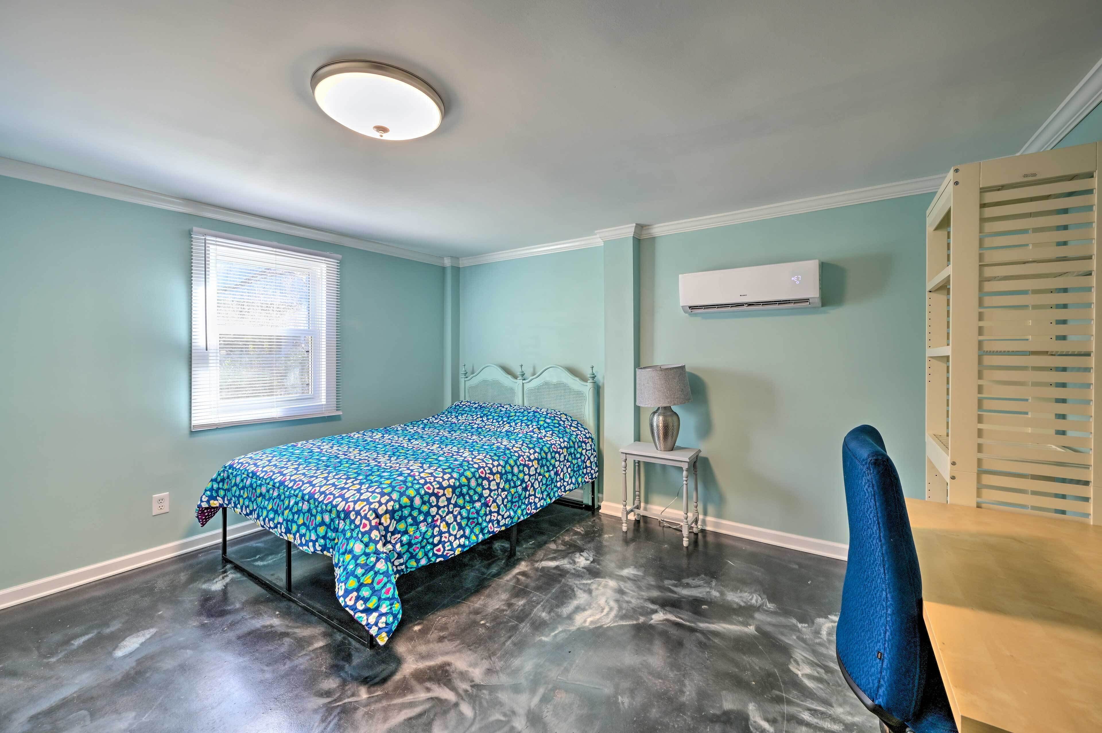 Quarto com cama, escrivaninha, cadeira, janela e ar condicionado.
