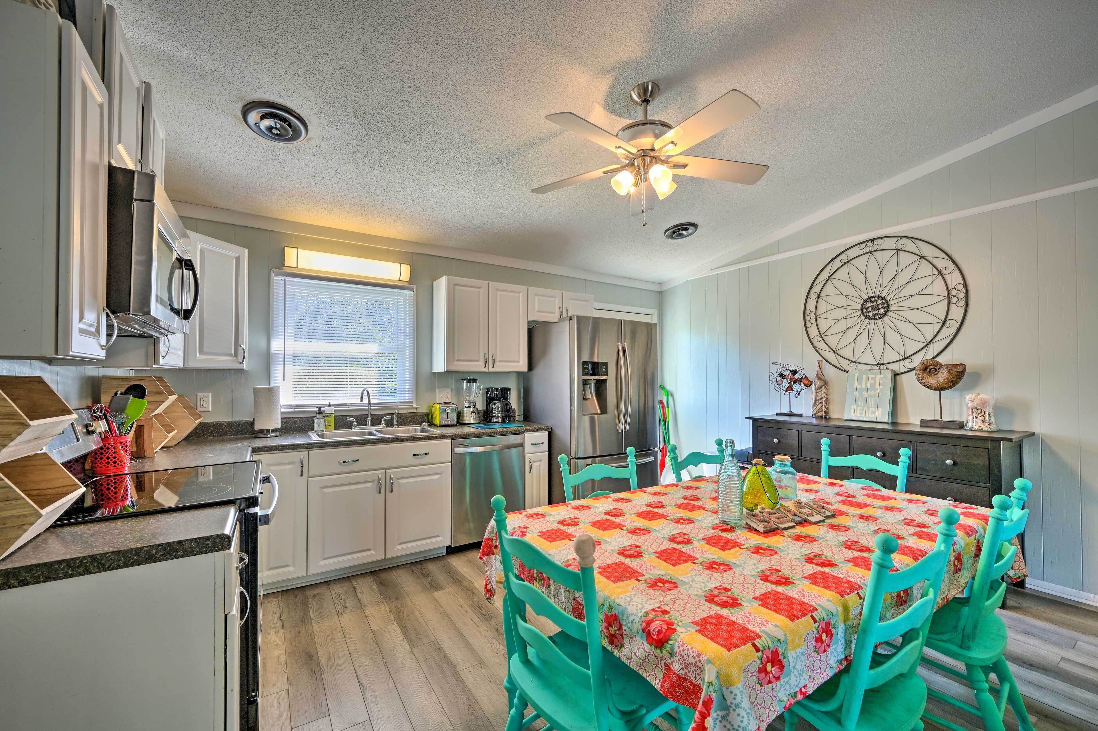 A kitchen with white cabinets, a stainless steel refrigerator, and a dining table with teal chairs.