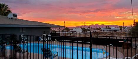 A swimming pool with lounge chairs and a fenced area, surrounded by a residential neighborhood with houses and mountains in the background.