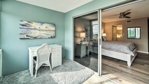 Une chambre à coucher comprenant un lit, un bureau, une chaise, un tableau et une porte-fenêtre coulissante donnant sur une autre pièce.