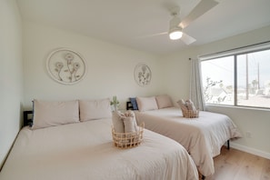 A hotel room with two beds, a ceiling fan, and a large window with a view.