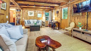 A wooden cabin interior with a sofa, coffee table, TV, and a desk with a chair. - Hike to the Coast! Log Cabin on 5 Acres in Bandon (Bandon)