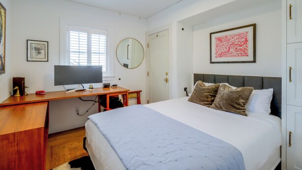 Een slaapkamer met een bed, een bureau, een televisie, een spiegel en een lijst met een kaart aan de muur.