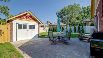 A patio with a brick floor, a table with chairs, and a barbecue grill.